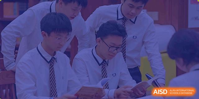 Close-up of several male students from Cogdel Cranleigh High School, dressed in white uniforms, leaning in together and collaborating on a task.