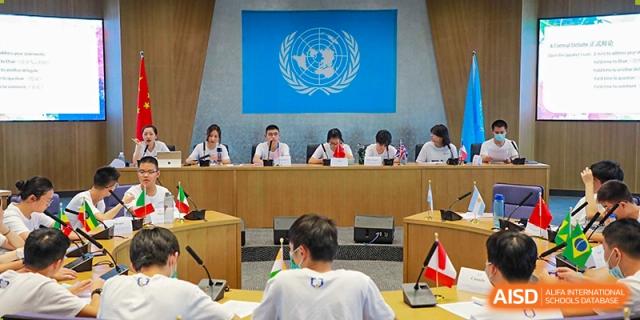 Students from Cogdel Cranleigh High School participating in a Model United Nations (MUN) or debate session, seated at a panel under the UN flag.