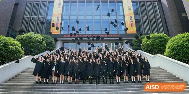 A large group of graduating students from Cogdel Cranleigh High School, dressed in black gowns and caps, posing outdoors on stairs.