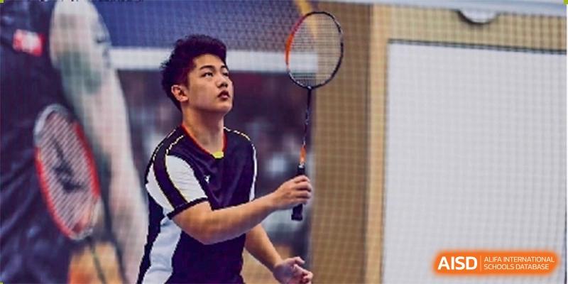 Cogdel Cranleigh High School student in a yellow and black uniform focusing on a shuttlecock while holding a badminton racket on a court.