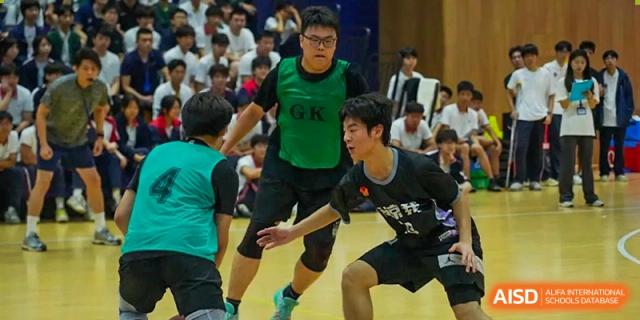 Two Cogdel Cranleigh High School students playing basketball; one in a green "GK" jersey defending another student in a black jersey.