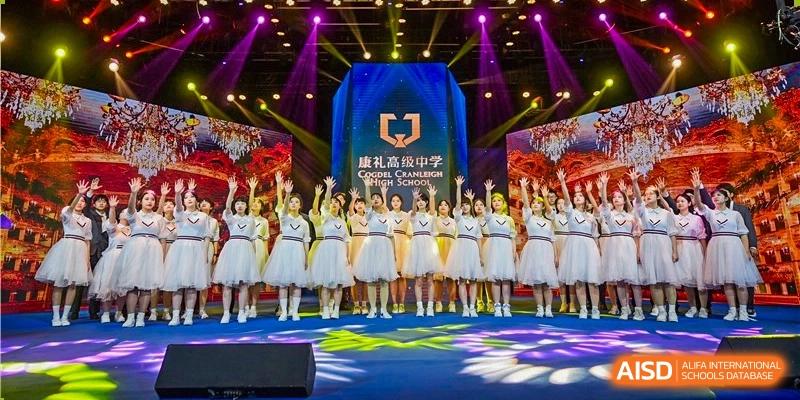 A large group of students from Cogdel Cranleigh High School dressed in white and gold performance outfits standing on a stage at an event.