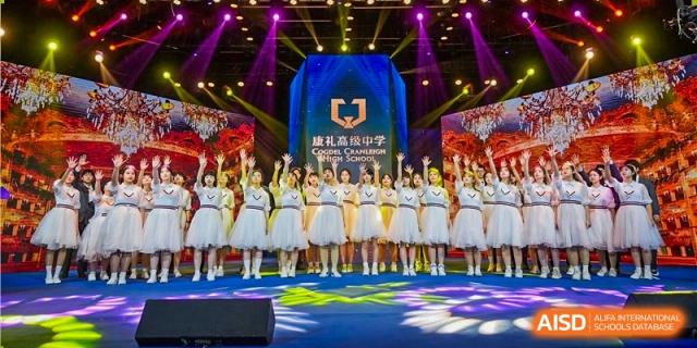 A large group of students from Cogdel Cranleigh High School dressed in white and gold performance outfits standing on a stage at an event.