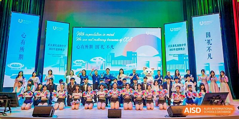 A group of students and teachers from Cogdel Cranleigh High School posing for a photo on a stage with a large screen backdrop featuring the school's name and skyline graphics.