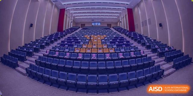 Interior view of the large auditorium at Cogdel Cranleigh High School, showing rows of empty blue seats facing a stage.