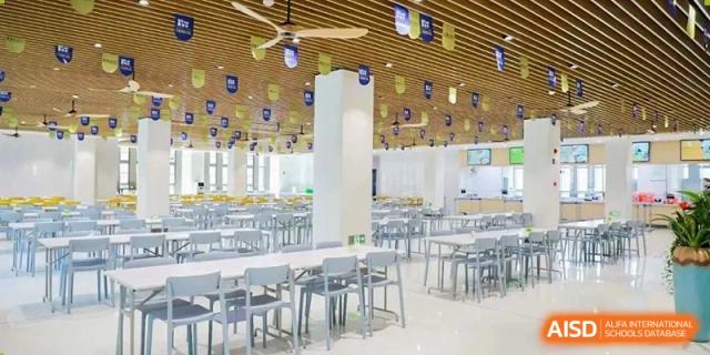 Another view of the spacious and modern cafeteria at Cogdel Cranleigh High School, showing an area with grey tables and chairs and decorative ceiling banners.