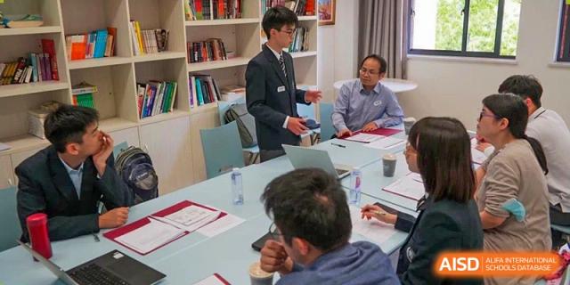 A teacher speaking to students seated at a conference table in a classroom at Fudan International School.