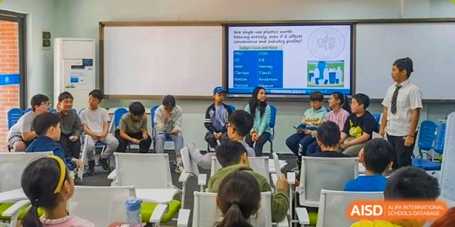 Students gathered for a presentation or class discussion with text projected onto a screen behind them at Fudan International School.