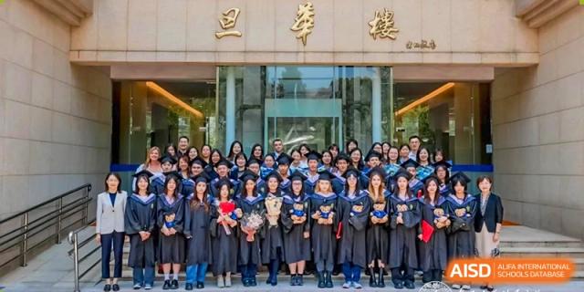 A large group of graduating students in caps and gowns posing together outside the building at Fudan International School.