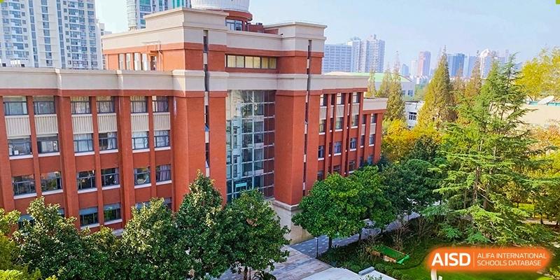 The brick and stucco exterior building and grounds of Fudan International School on a sunny day.
