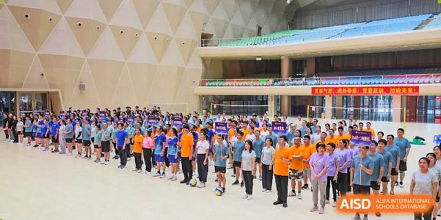 A large group of students from Humen Foreign Language School International Division in different colored shirts stand together in an indoor assembly or performance area.