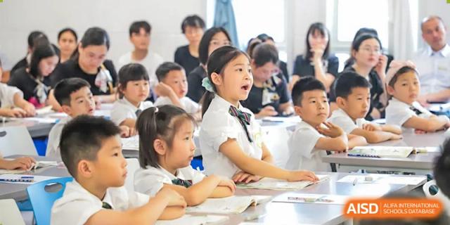 Students from Humen Foreign Language School International Division in white uniforms sit in a classroom, attentively looking towards the front of the room.
