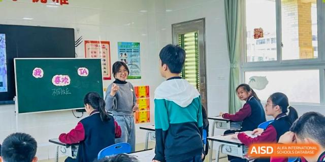 A student from Humen Foreign Language School International Division wearing a gray and light blue jacket stands in a classroom doorway, ready to enter or exit.
