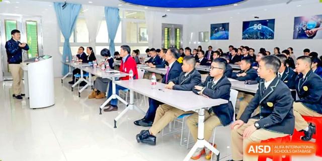 Teachers and administrators from Humen Foreign Language School International Division attend a meeting or conference in a brightly lit indoor venue, seated at long tables.