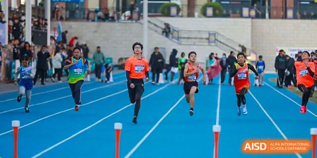 A runner from Humen Foreign Language School International Division in a bright orange top and black shorts sprints down an outdoor track during a race.