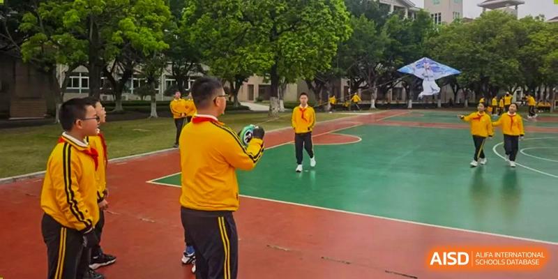 Students from Humen Foreign Language School International Division in yellow shirts are on an outdoor basketball court, with one student holding a ball, practicing sports.