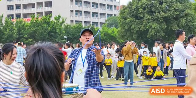 A teacher or student from Humen Foreign Language School International Division enthusiastically leads an activity outdoors while holding a small baton.