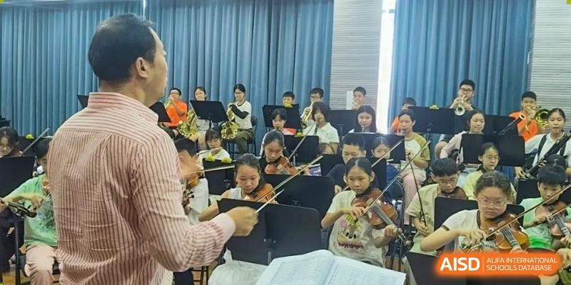 Students from Humen Foreign Language School International Division practice their instruments in a classroom setting, being directed by a teacher or conductor.