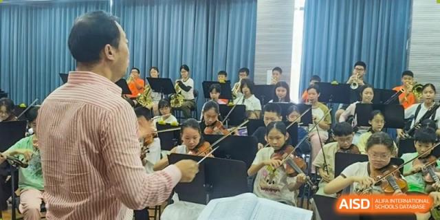 Students from Humen Foreign Language School International Division practice their instruments in a classroom setting, being directed by a teacher or conductor.