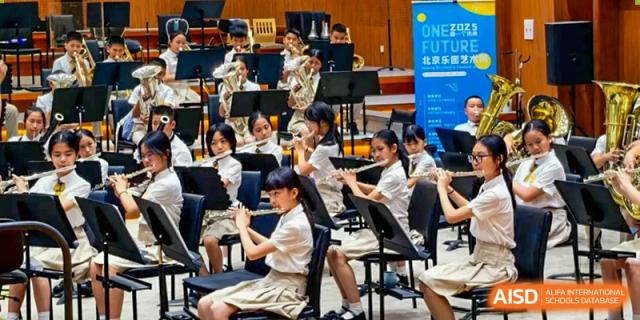 A large group of students from Humen Foreign Language School International Division wearing school uniforms play instruments in a school band or orchestra performance.