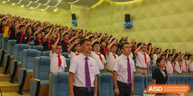 Students from Humen Foreign Language School International Division stand in a group, singing or raising their hands in unison during an assembly or performance.