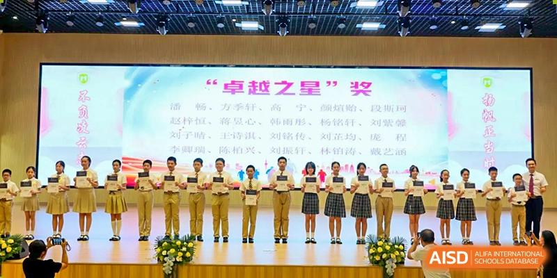 A group of students from Humen Foreign Language School International Division stand on a stage for an awards ceremony beneath a banner with Chinese text.