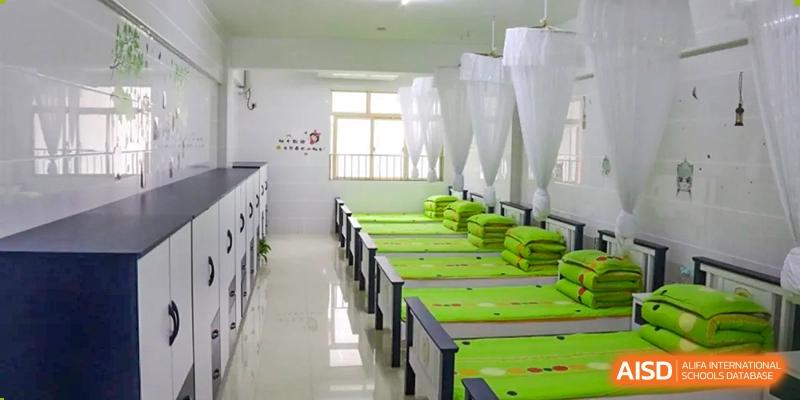 A clean, well-lit dormitory room at Humen Foreign Language School International Division with multiple beds covered in bright green bedding and white mosquito nets.