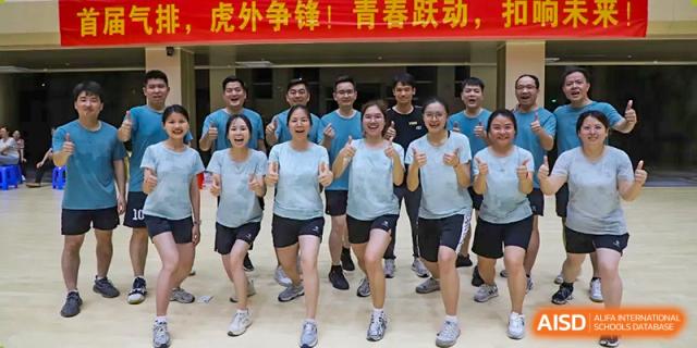 A group of adults from Humen Foreign Language School International Division in matching light blue shirts and black shorts jogging together during a school sports event.
