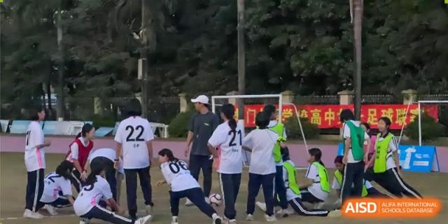 Female students from Humen Foreign Language School International Division in uniforms with numbers '22' and '21' playing a team sport outdoors, possibly soccer or football.