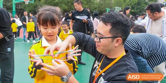 An adult from Humen Foreign Language School International Division helps a young female student with a hands-on activity outdoors.
