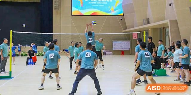 A male student from Humen Foreign Language School International Division wearing a blue jersey with number '01' jumps to hit a volleyball over the net during a game.