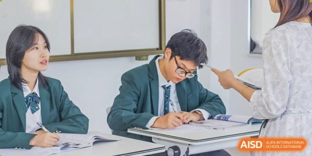 A male student from Maple Glory Education in a blazer writing diligently at his desk in a classroom.