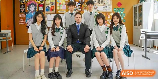 A male instructor in a suit sitting with a group of Maple Glory Education students in their school uniforms.