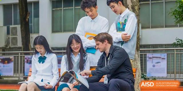 A foreign male teacher from Maple Glory Education interacting with and assisting two students in a classroom.