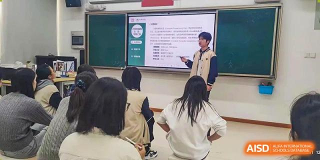 A Maple Glory Education student giving a presentation in front of a class, pointing at a projected slide.
