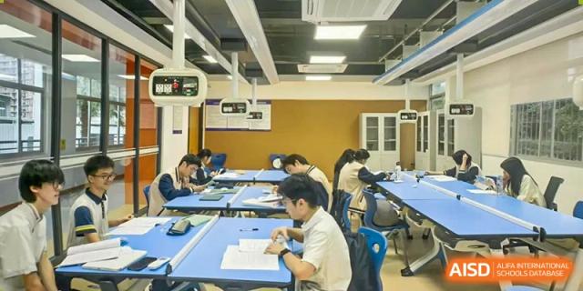 Maple Glory Education students taking a test or focused on written assignments in a large, well-lit classroom.