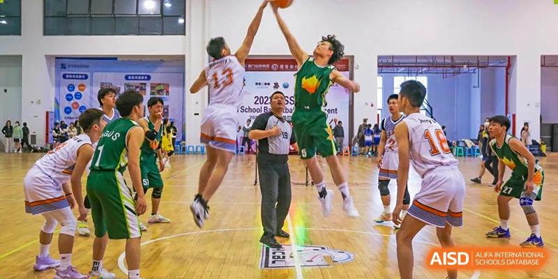 An action shot of two Maple Glory Education players jumping high for a rebound during a basketball game, with a referee watching.