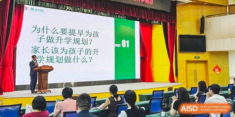 A large screen displaying Chinese text during an event, with students from Maple Glory Education seated and watching in an auditorium.