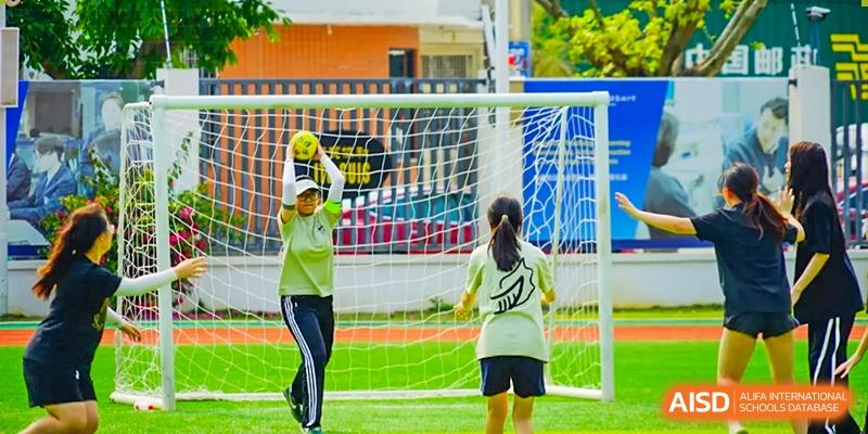 Female students from Maple Glory Education in matching green uniforms playing handball or a similar sport near a goal net.