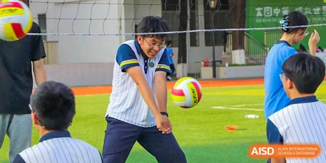 A male student from Maple Glory Education hitting a volleyball with a strong forearm pass on an outdoor turf court.