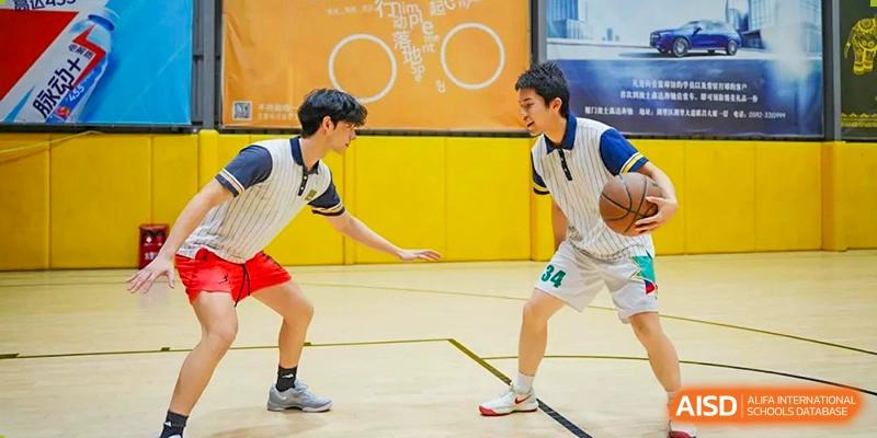 Two male students from Maple Glory Education playing basketball on an outdoor court, one holding the ball.