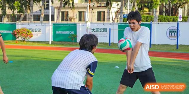 Two students from Maple Glory Education passing a volleyball back and forth on an outdoor sports field.