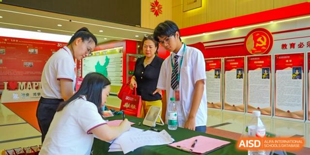 A student in uniform signing a document or form at a table with an adult present at Maple Leaf International School Wuhan.
