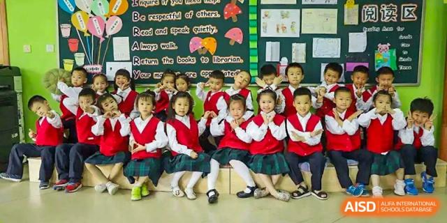 A group of young students in red and white uniforms seated on the floor in a brightly decorated classroom at Maple Leaf International School Wuhan.