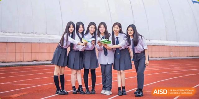 A group of six female students in uniforms smiling and posing outdoors on the school track at Maple Leaf International School Wuhan.