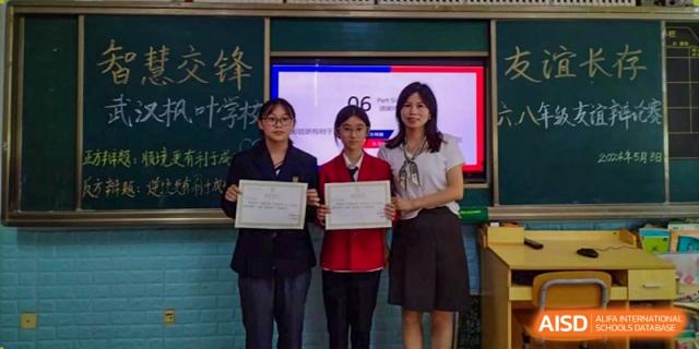 Two female students receiving certificates or awards from a teacher in a classroom at Maple Leaf International School Wuhan.