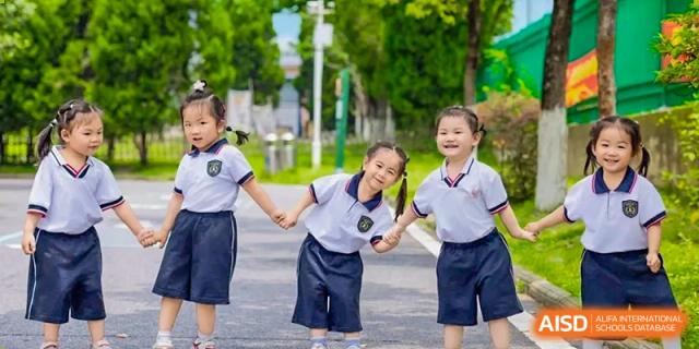 Two young female students and a male student in school uniform smiling and holding hands outdoors at Maple Leaf International School Wuhan.