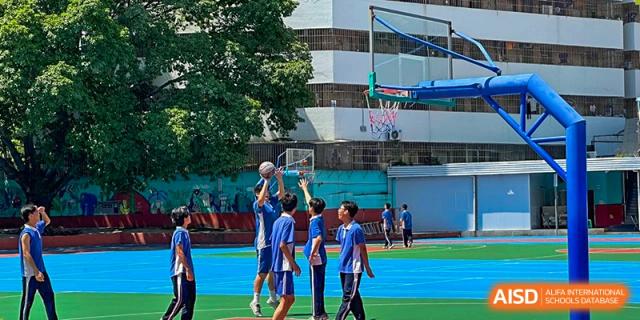 Students in blue shirts playing a basketball game on the outdoor court, with a close-up of the net in the background, at Maple Leaf International School Wuhan.