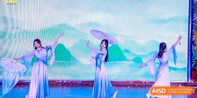 A student in traditional attire performing a graceful fan or umbrella dance on a brightly lit stage at Maple Leaf International School Wuhan.