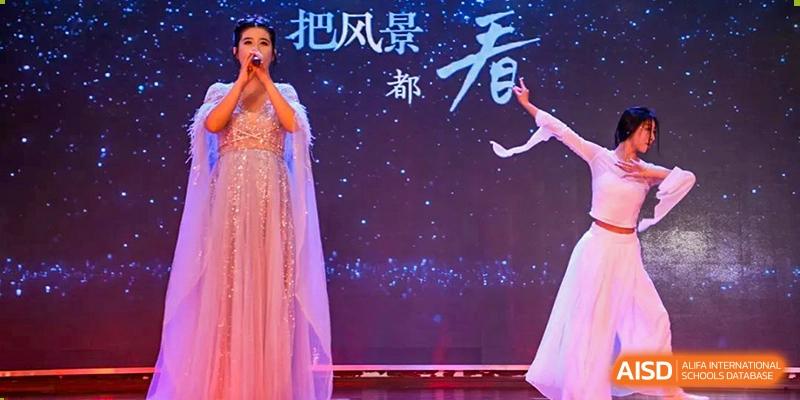 A female student in a sparkling pink gown singing on a dark stage with star-like lights in the background at Maple Leaf International School Wuhan.